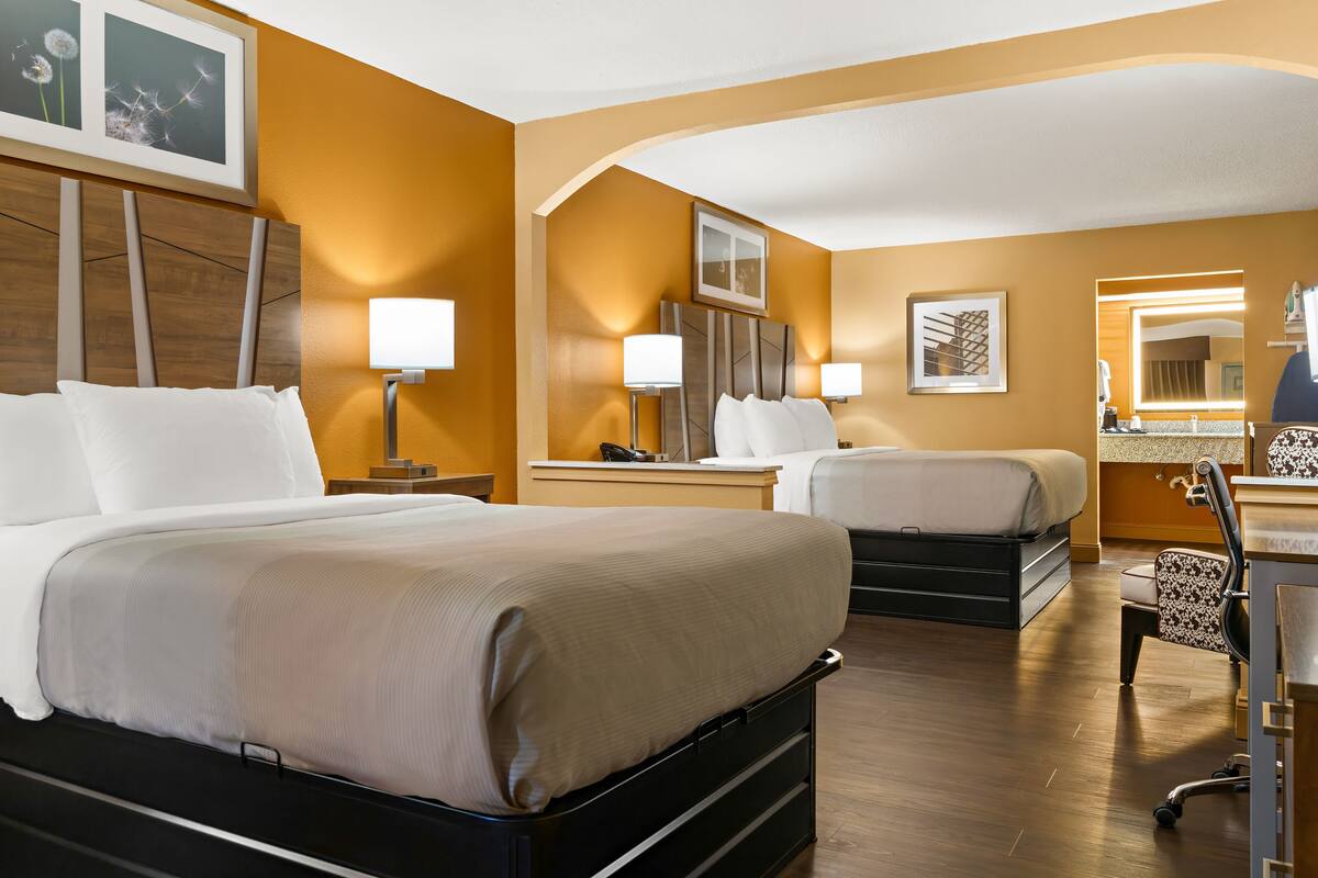 Ett hotellrum med två sängar, ett skrivbord, en stol och en spegel.