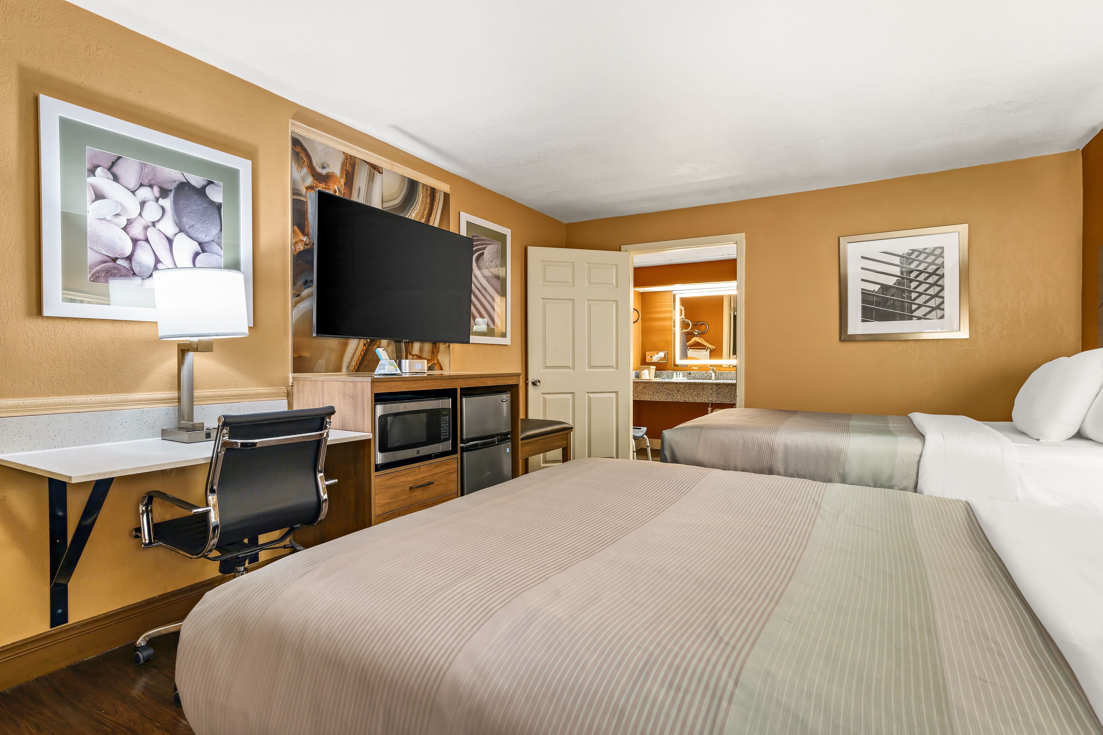 Une chambre d’hôtel avec deux lits, un bureau avec une chaise, une télévision et une kitchenette.
