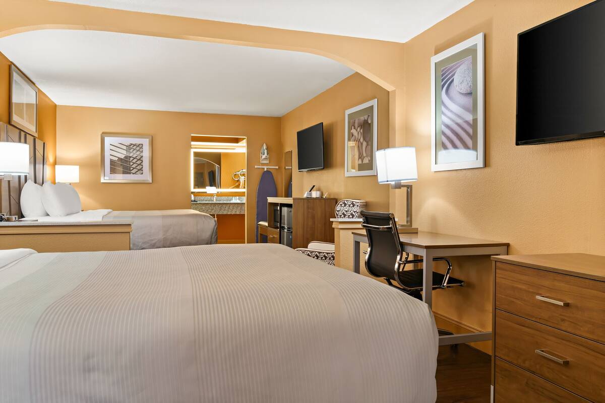 Ett hotellrum med en stor säng, ett skrivbord med en stol, en TV och ett badrum med spegel och handfat.