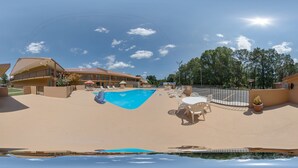A pool area with a clear blue pool, lounge chairs, and a building with a red roof.