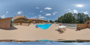 A pool area with a clear blue pool, lounge chairs, and a building with a red roof.