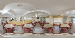 A spacious dining area with multiple tables and chairs, a kitchen area, and a counter with a cash register.