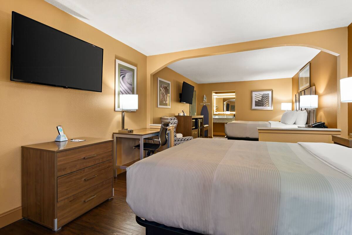 Ett hotellrum med en säng, ett skrivbord, en stol, en byrå, en tv och en spegel på badrummet.