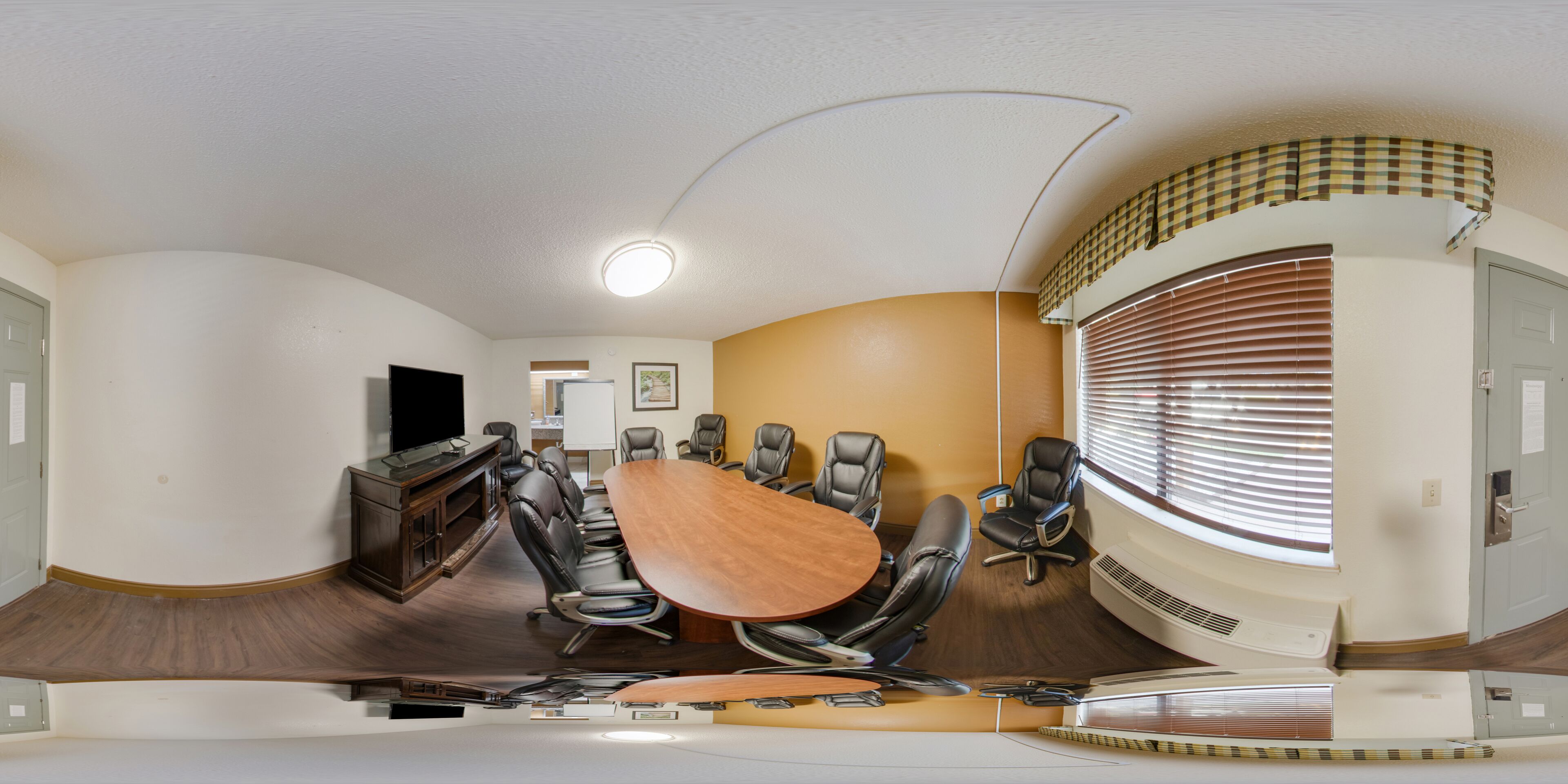 A conference room with a large oval table, leather chairs, a television, and a ceiling light.