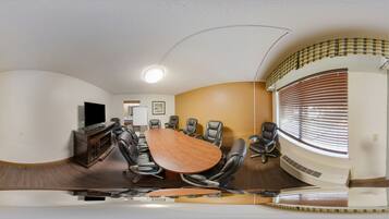 A conference room with a large oval table, leather chairs, a television, and a ceiling light.
