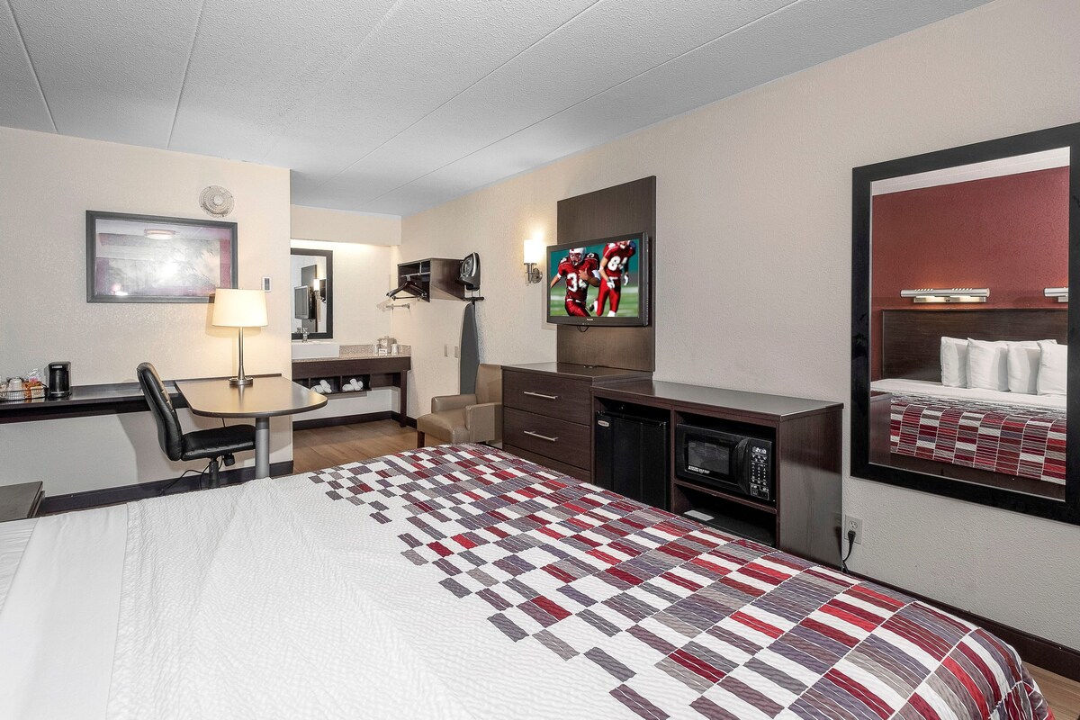 A hotel room with a bed, desk, chair, television, and a microwave.