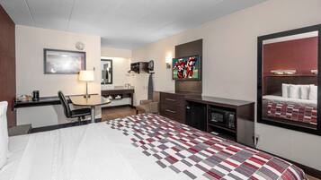 A hotel room with a bed, desk, chair, television, and a microwave.