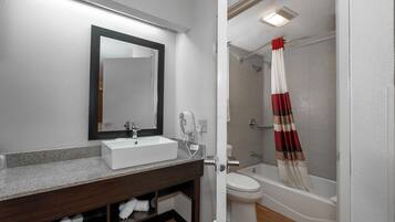 Un baño con lavamanos, espejo, toallero, inodoro y zona de ducha.