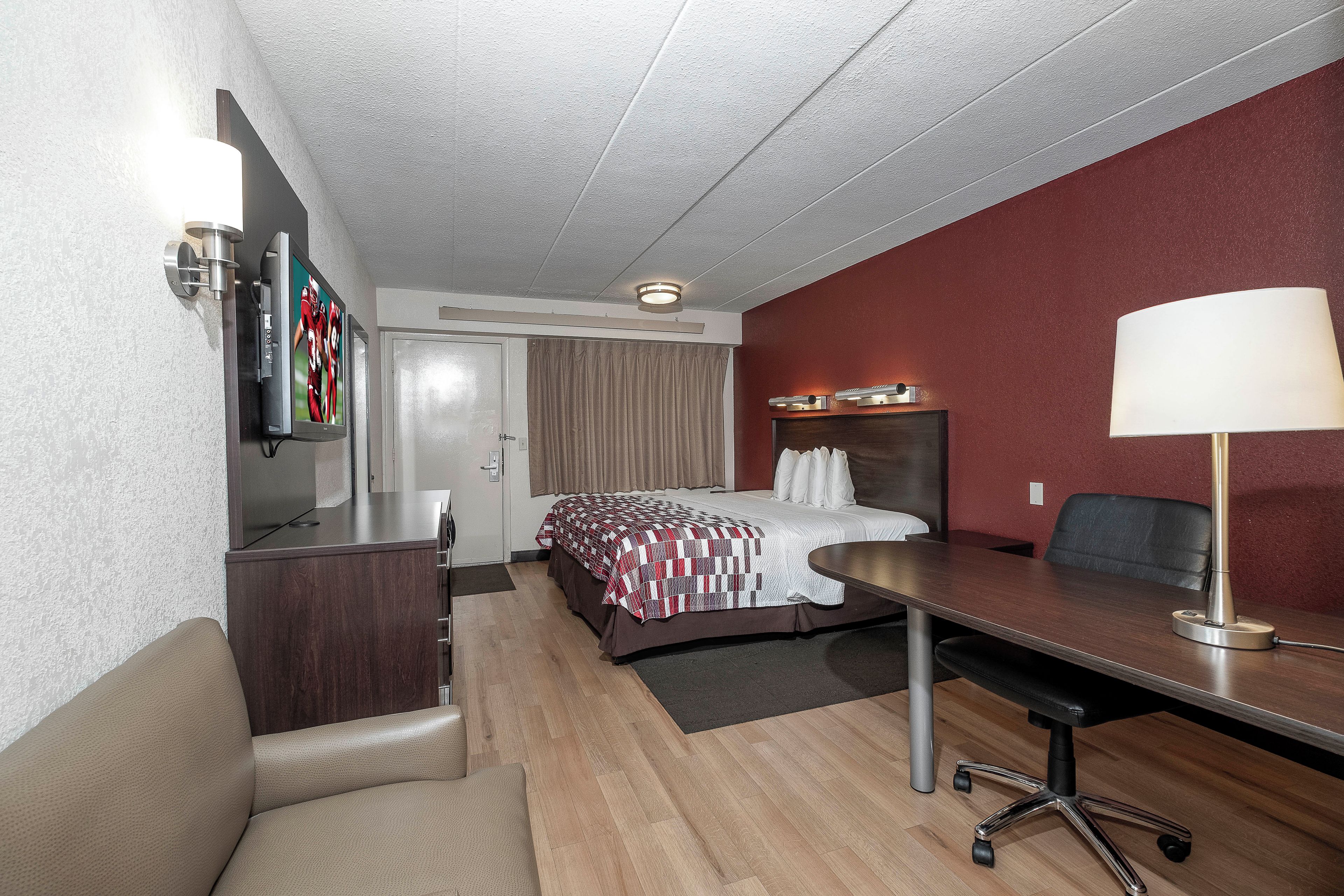 A hotel room with a bed, desk, chair, TV, and a lamp.