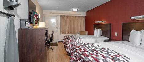 Una habitación de hotel con dos camas, un escritorio con computadora, televisor y espejo.