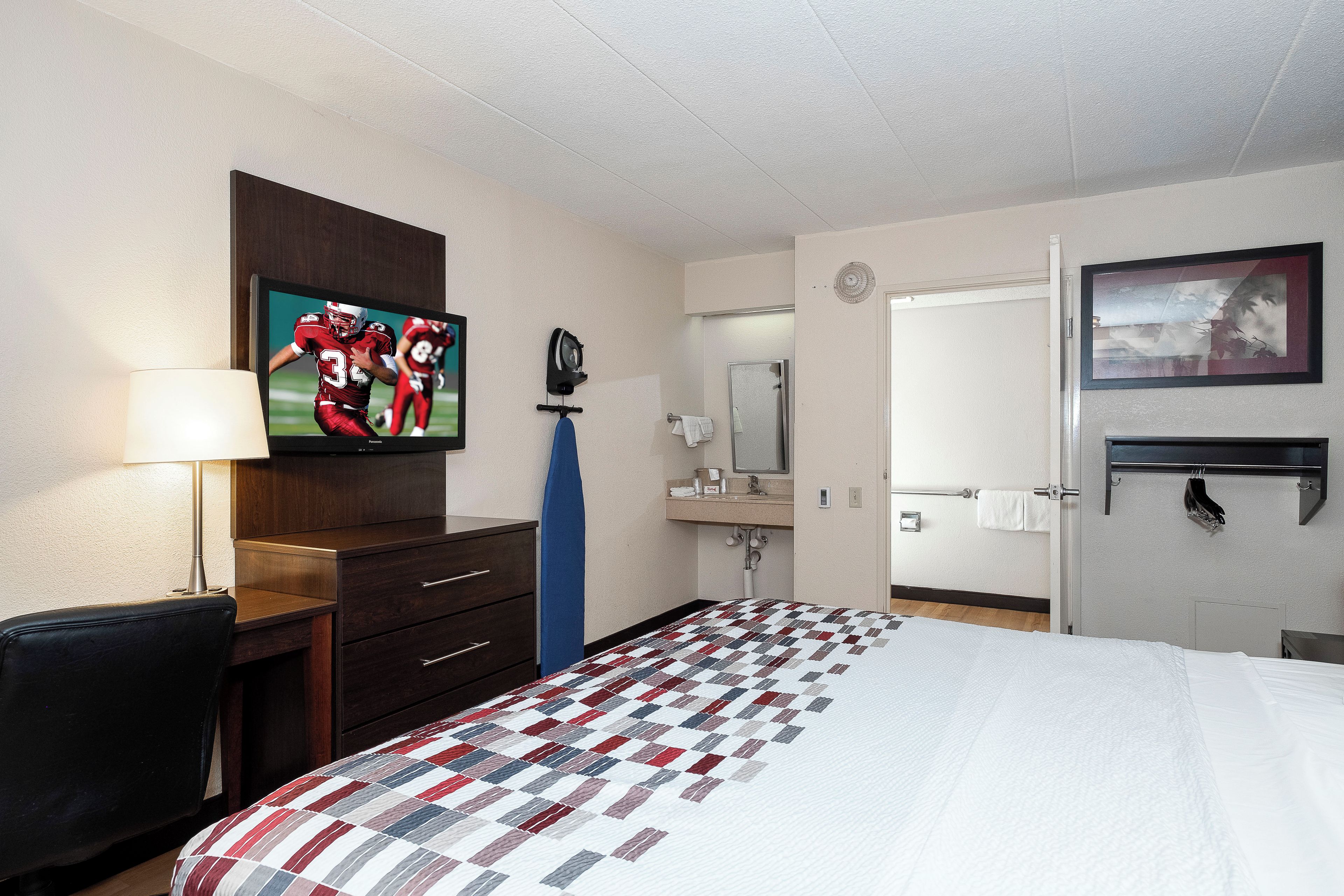 A hotel room with a bed, a desk, a television, a mirror, and a bathroom door.