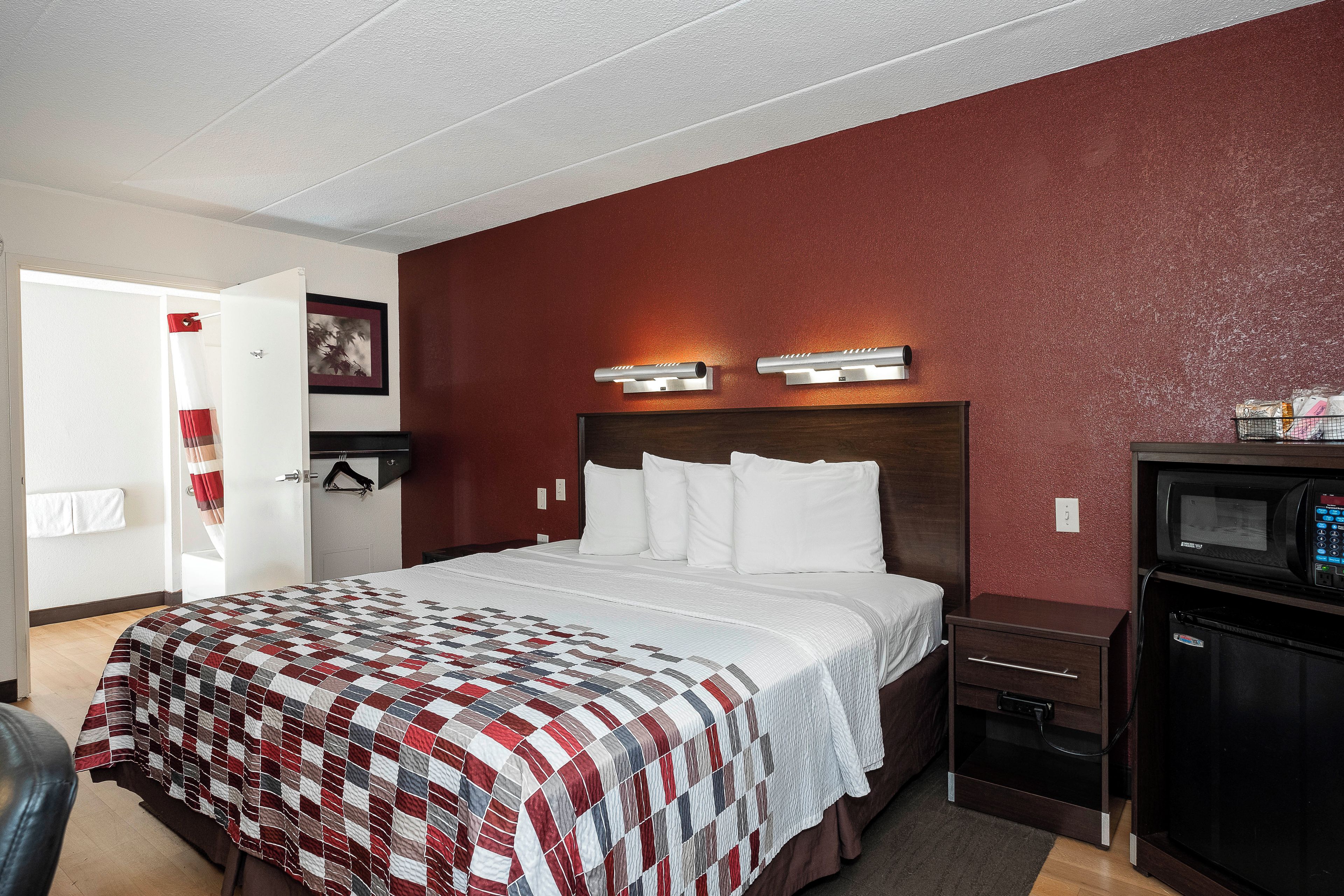 A hotel room with a bed, a nightstand, a microwave, and a red accent wall.