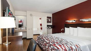 Habitación de hotel con cama, escritorio, silla, televisión y baño visible a través de una puerta abierta.