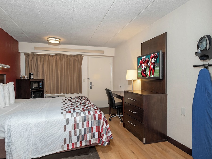Quarto de hotel com cama, escrivaninha, televisão e guarda-roupa.
