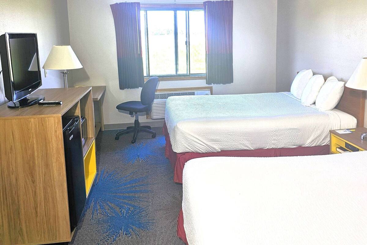 Habitación de hotel con cama, escritorio con televisor y control remoto, una silla y una ventana con cortinas.