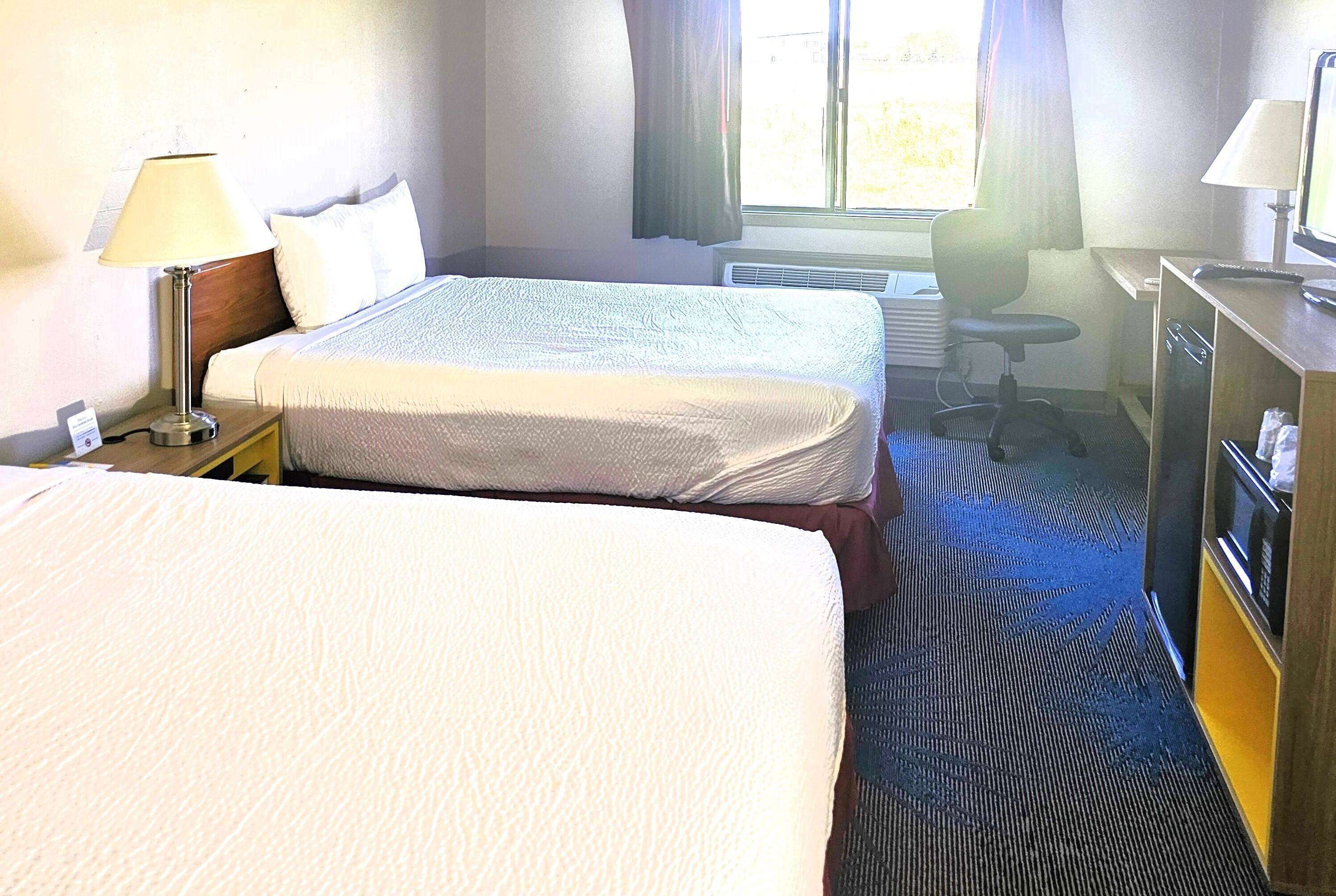 A hotel room with two beds, a desk, a chair, a lamp, and a desk lamp.