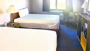 A hotel room with two beds, a desk, a chair, a lamp, and a desk lamp.