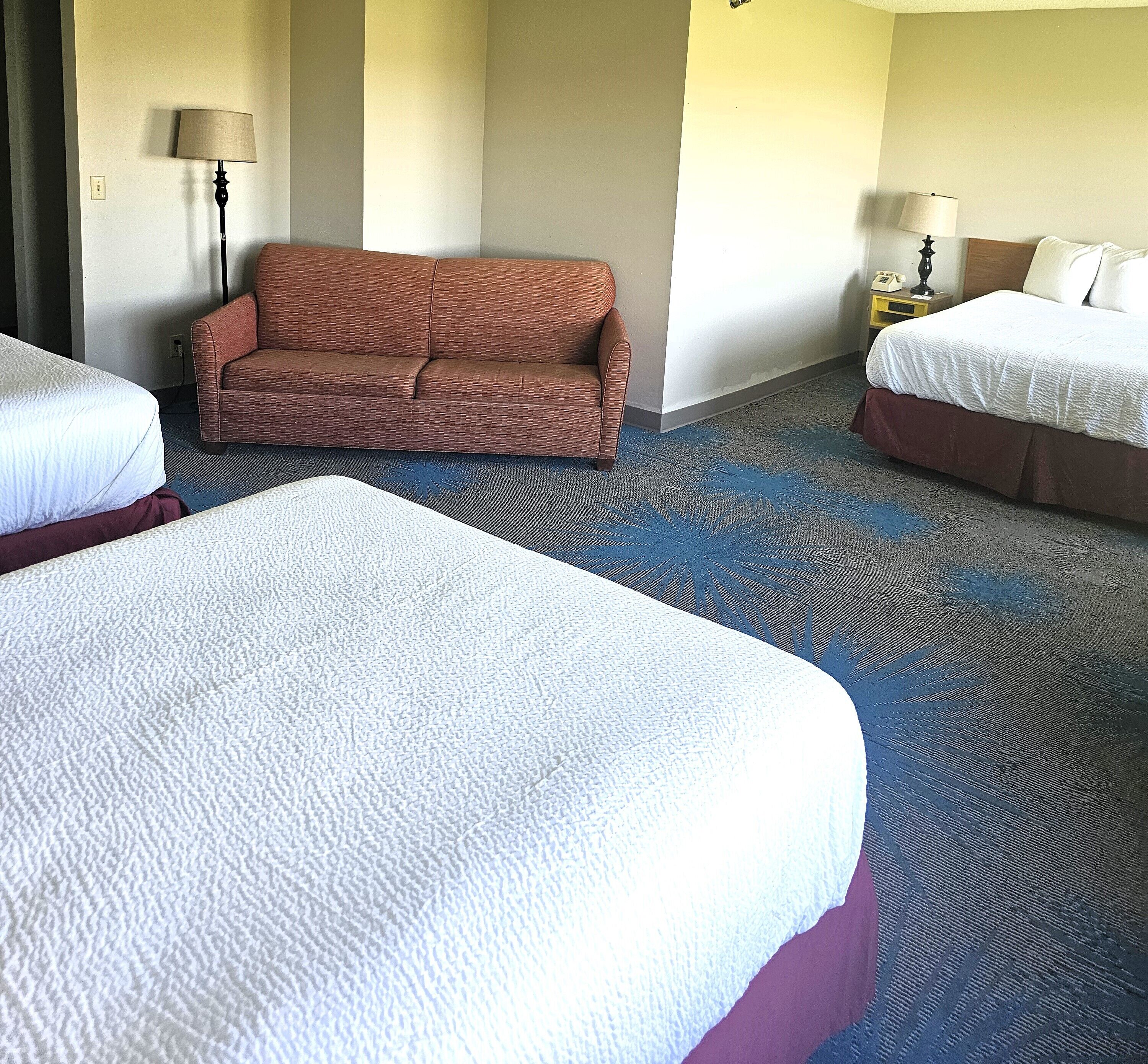 A hotel room with two beds, a sofa, and a carpeted floor.