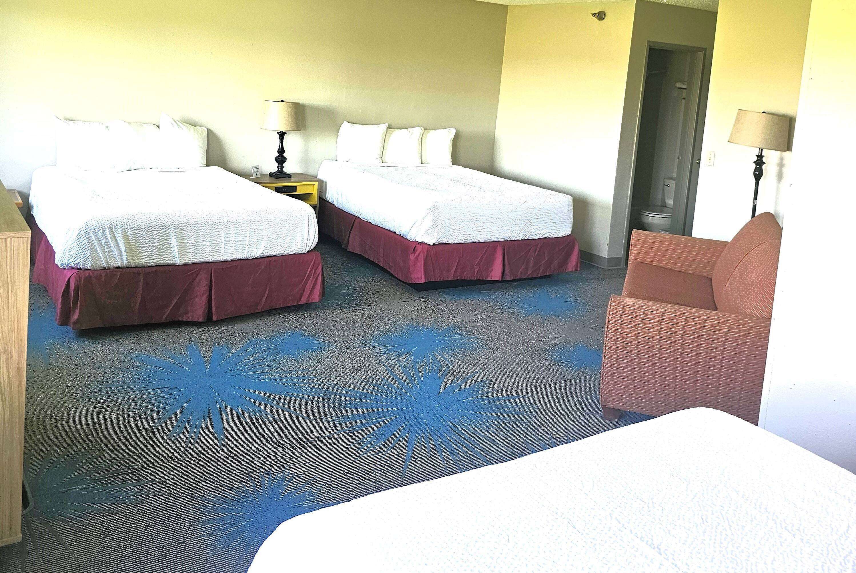 A hotel room with two beds, a chair, and a bathroom door.