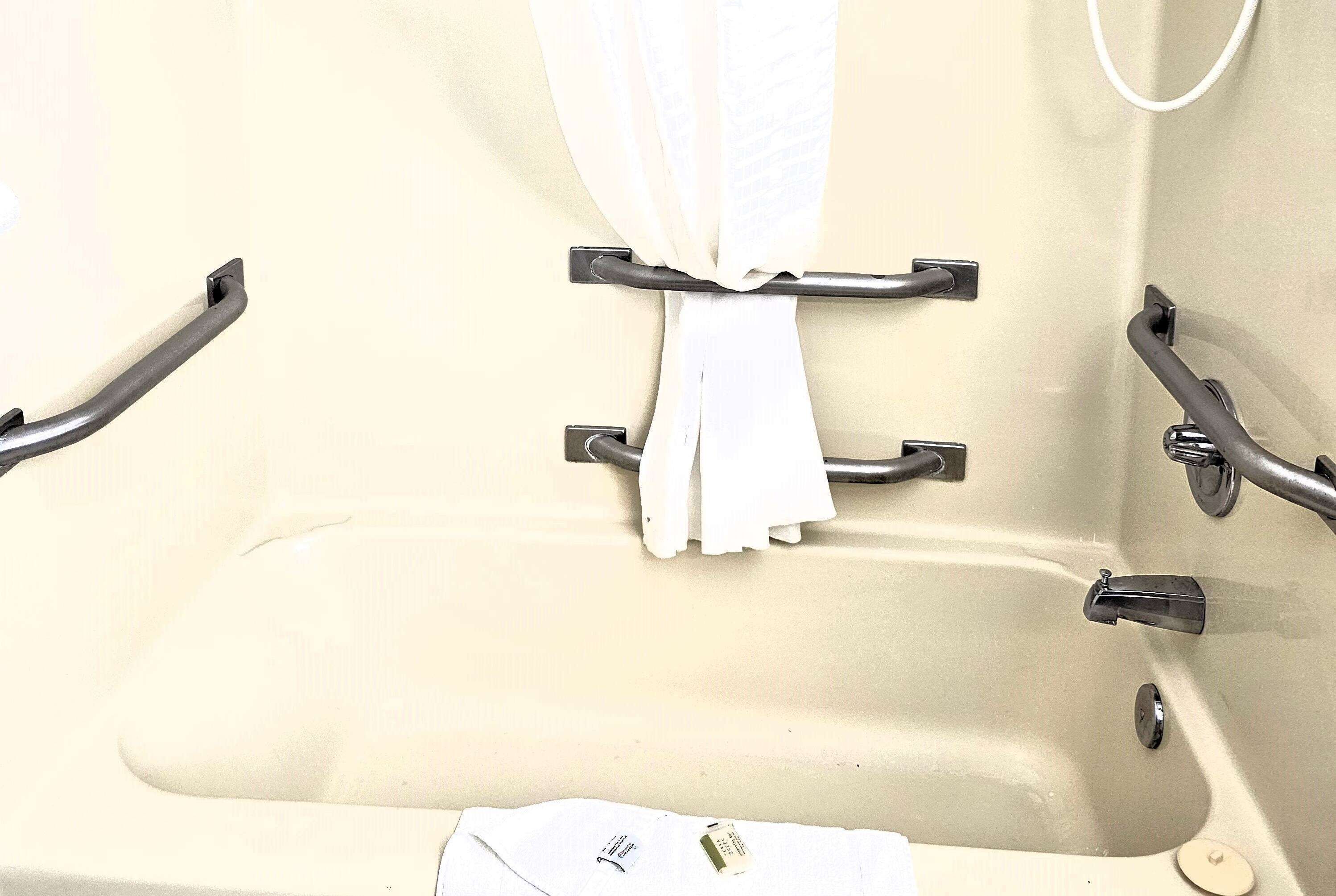 A bathtub with grab bars, a towel rack, and a handheld showerhead.