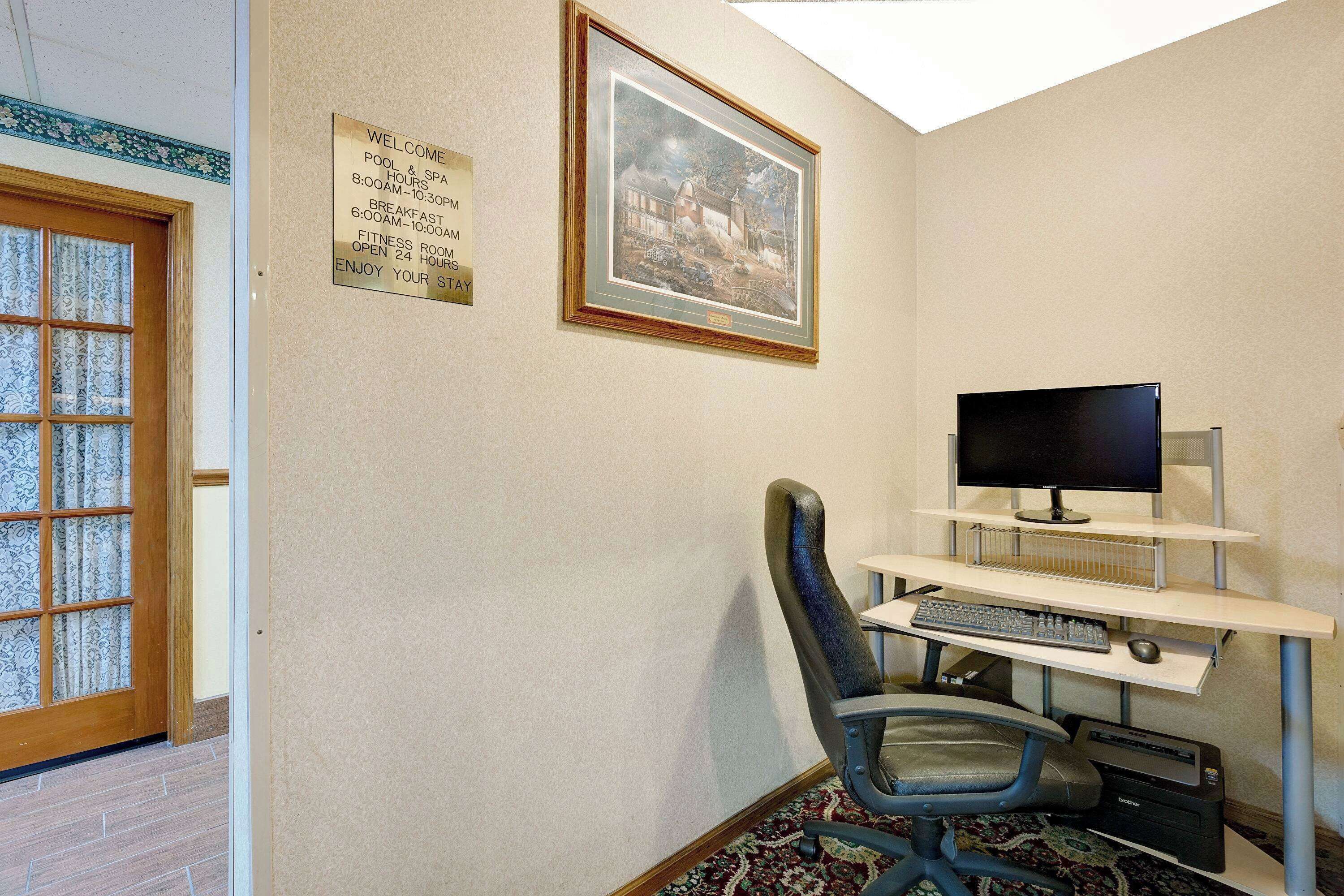 A room with a desk, computer, and chair. There is a framed picture on the wall and a sign with room information.