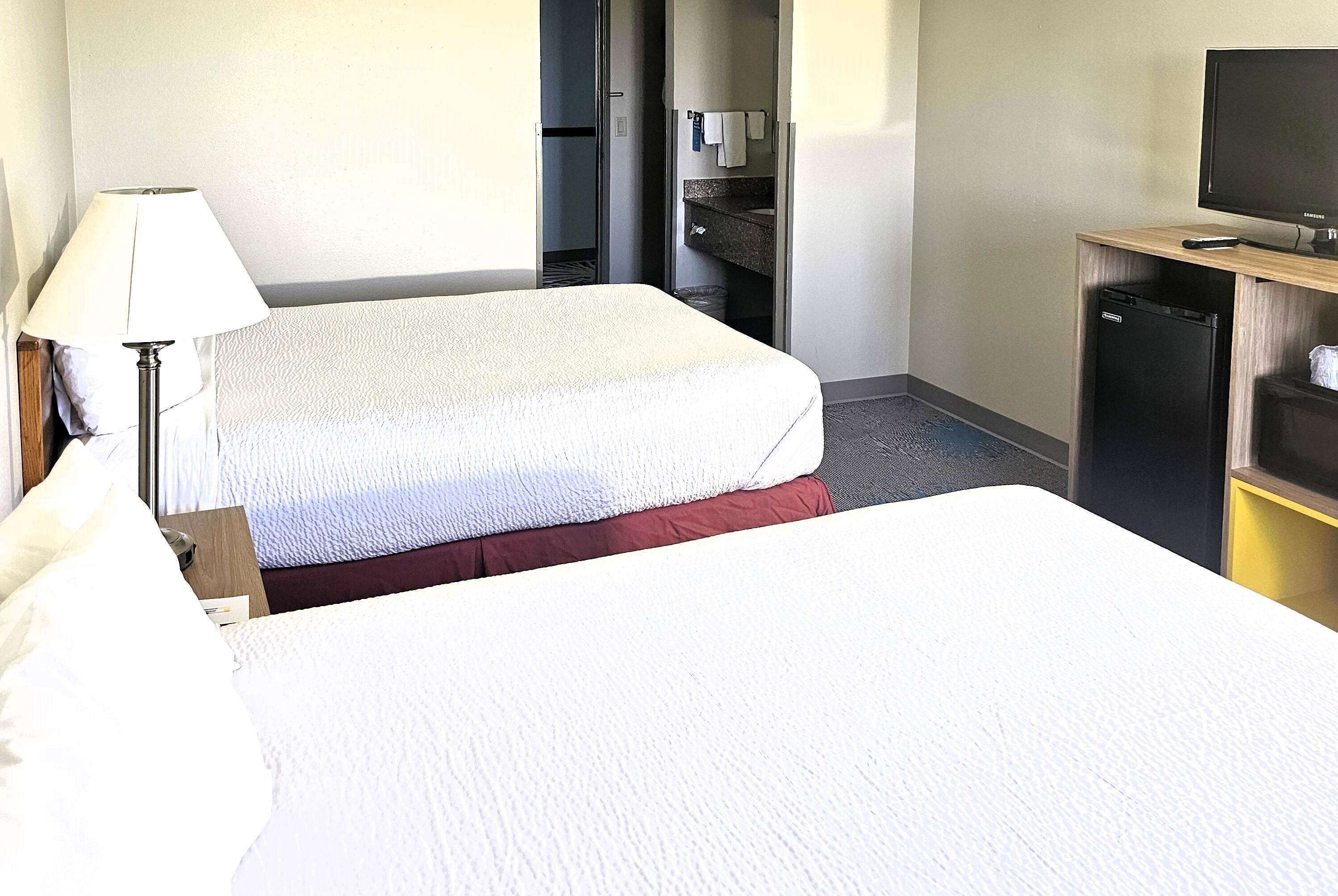 A hotel room with two beds, a desk with a lamp, a television, and a small refrigerator.