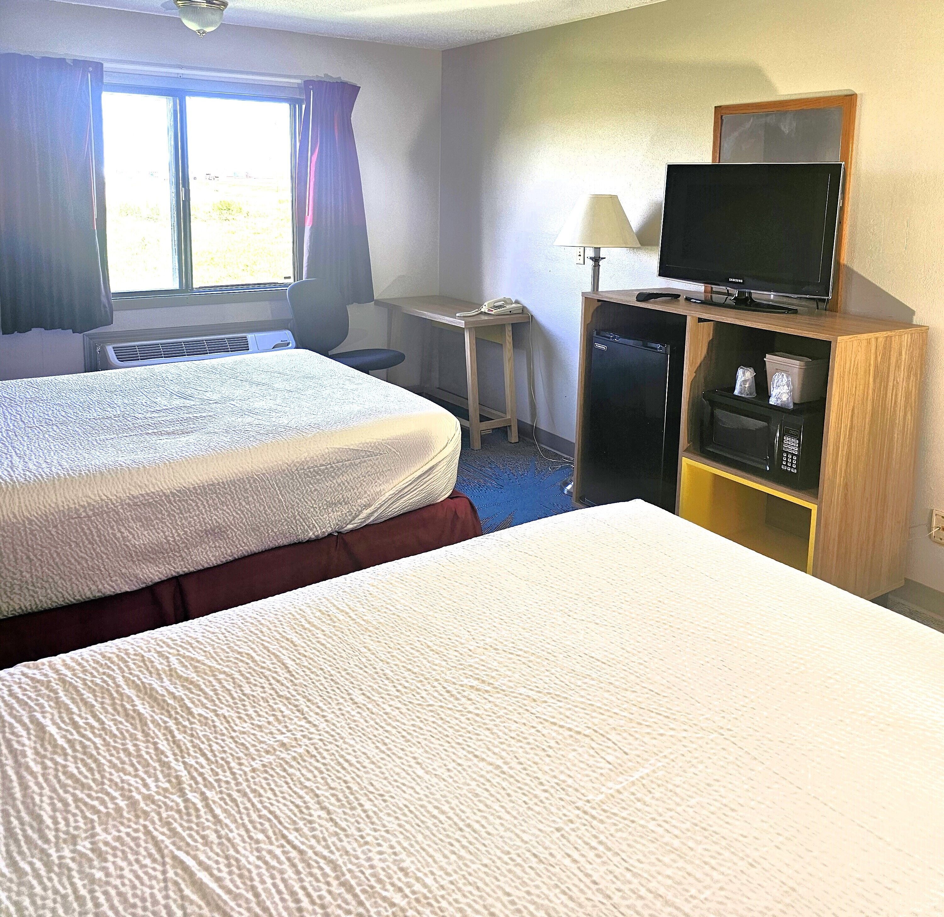 Una habitación de hotel con dos camas, un escritorio con lámpara, televisión y refrigerador.