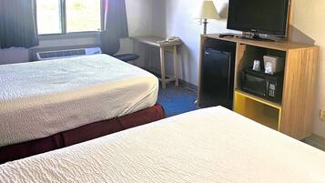 Una habitación de hotel con dos camas, un escritorio con lámpara, televisión y refrigerador.