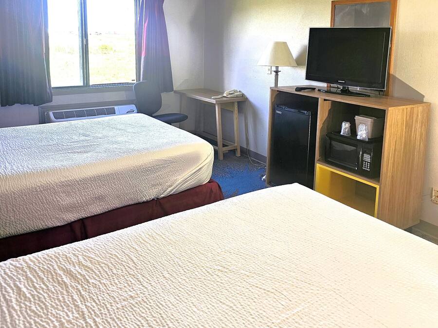 Una habitación de hotel con dos camas, un escritorio con lámpara, televisión y refrigerador.