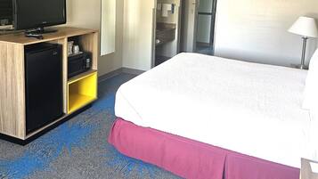 A hotel room with a bed, a desk with a television, a minibar, and a bathroom visible through an open door.