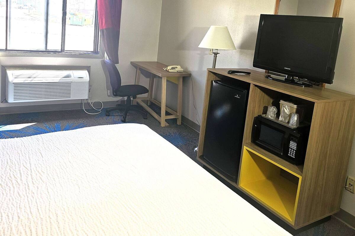 Una habitación de hotel con una cama, un escritorio con lámpara, televisión, refrigerador y microondas.
