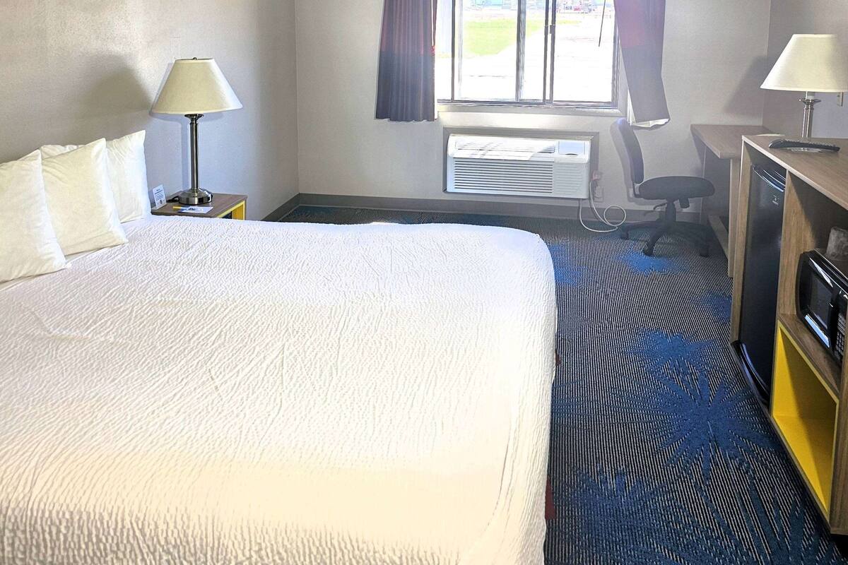 Habitación de hotel con una cama grande, dos lámparas de noche, un escritorio con una silla, un equipo de aire acondicionado y una ventana con cortinas.