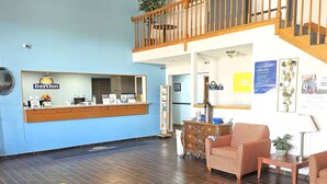 A reception area with a Days Inn sign, a wooden staircase, a reception desk, a sofa, and a coffee table.
