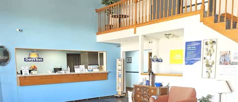 Zona de recepción con el letrero de Days Inn, una escalera de madera, un mostrador de recepción, un sofá y una mesa de centro.