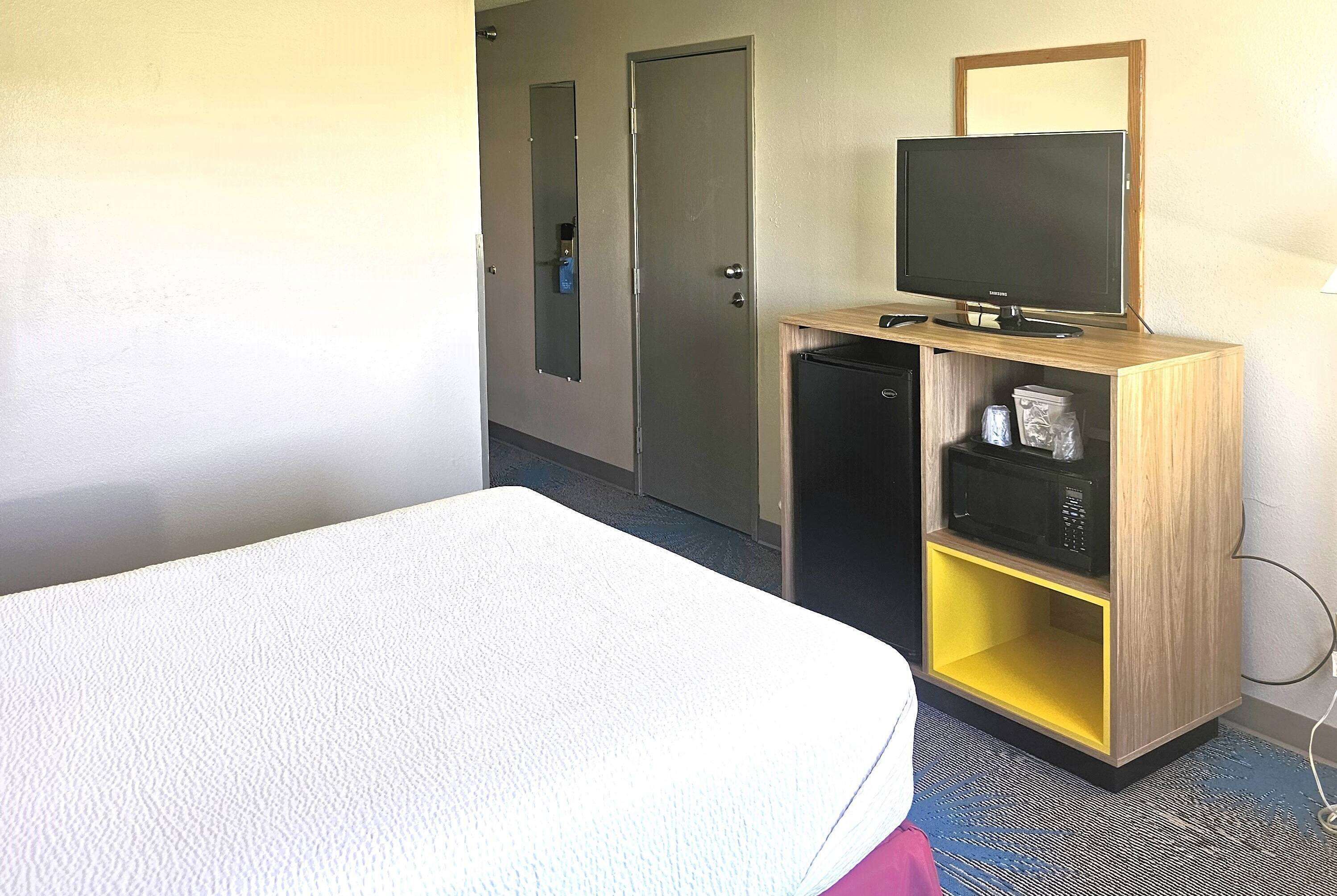 Une chambre d’hôtel avec un lit, un téléviseur posé sur un meuble en bois, un four à micro-ondes et une porte.
