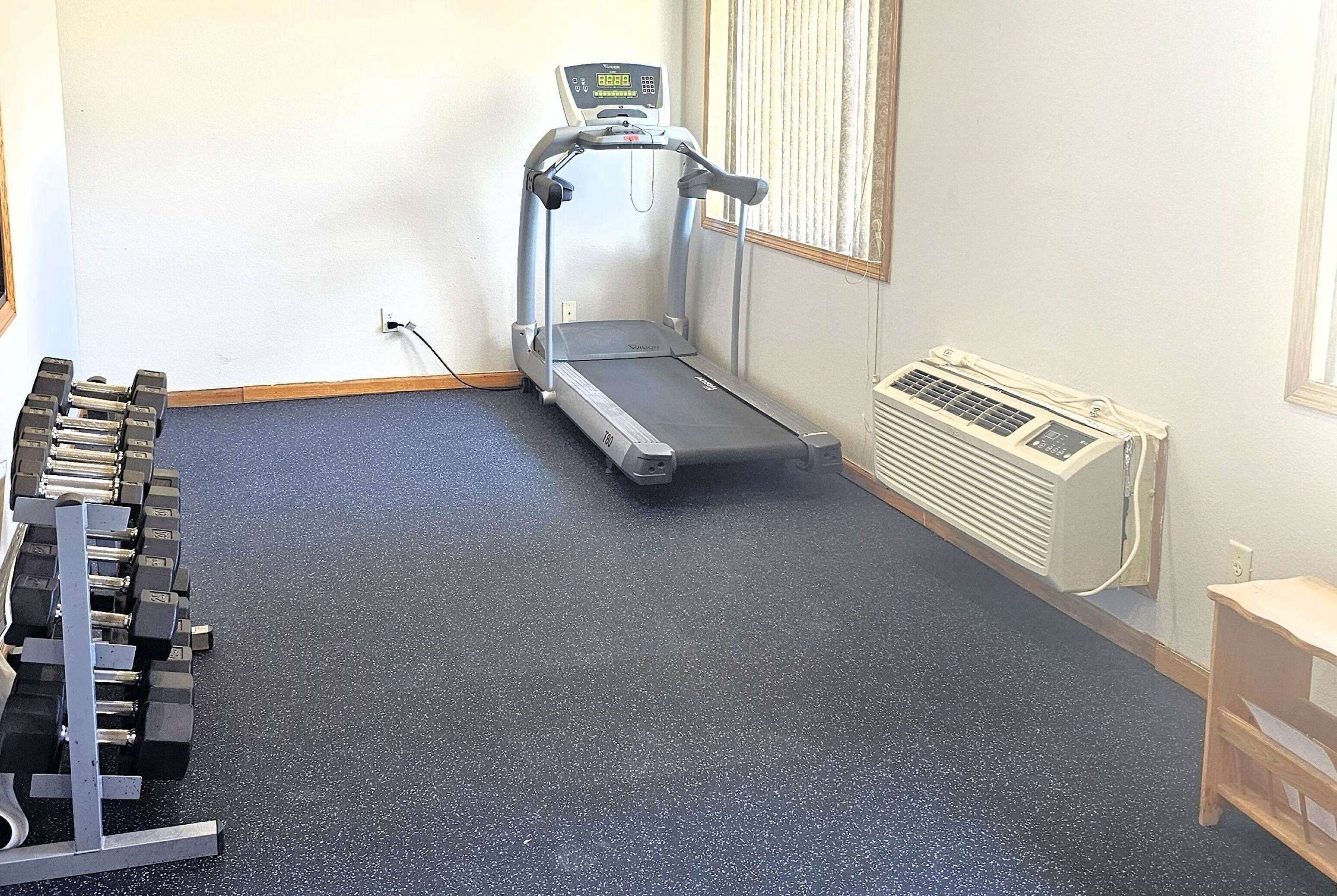 A room with a treadmill, a set of dumbbells, and a wall-mounted heater.