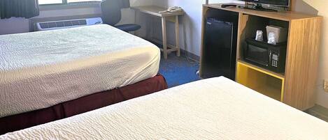 Habitación de hotel con dos camas, un escritorio con lámpara, televisor y microondas.