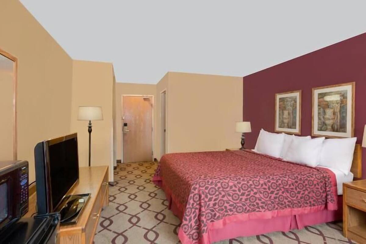 Una habitación de hotel con una cama, dos lámparas de noche, un televisor y un escritorio con lámpara.