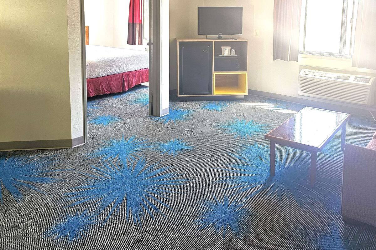 Una habitación de hotel con una cama, un televisor sobre un mueble bajo, una mesita y una alfombra con diseño azul.