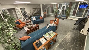 Un vaste espace de vie comprenant un canapé bleu, un fauteuil orange et une table basse avec des magazines. On aperçoit un escalier au fond, qui mène à un autre étage.