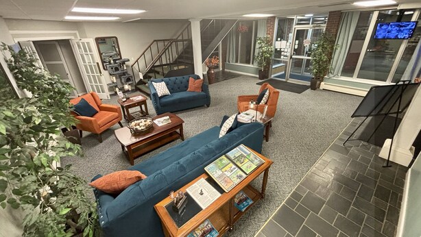 A spacious living area with a blue sofa, orange armchair, and a coffee table with magazines. A staircase is visible in the background, leading to another floor.
