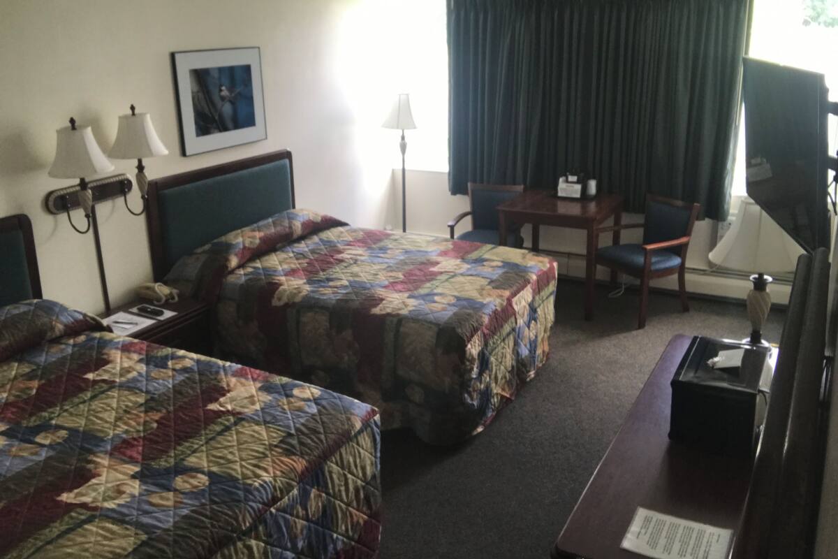 A hotel room with two beds, a desk, a chair, a TV, and a window with curtains.