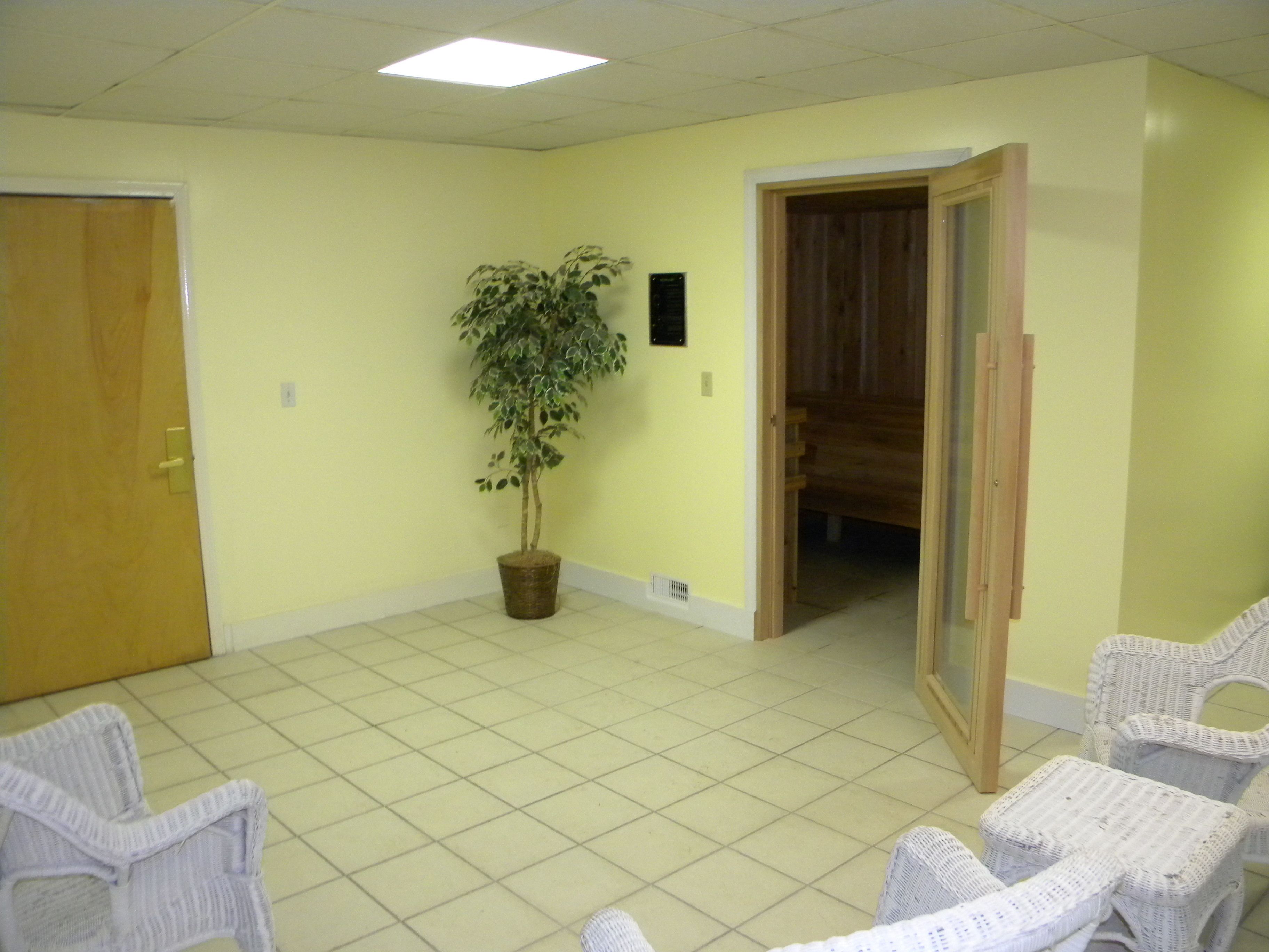 Une pièce avec un sol carrelé, une plante en pot, des chaises en osier et une porte en bois.