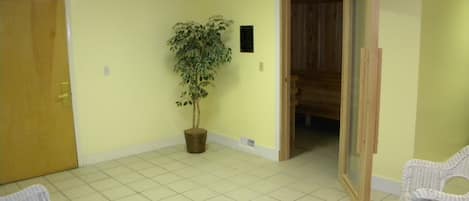 Une pièce avec un sol carrelé, une plante en pot, des chaises en osier et une porte en bois.