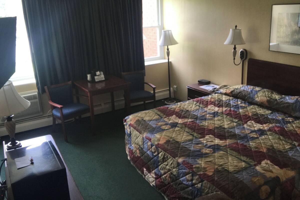 A hotel room with a bed, a desk, a chair, a lamp, and a window with curtains.