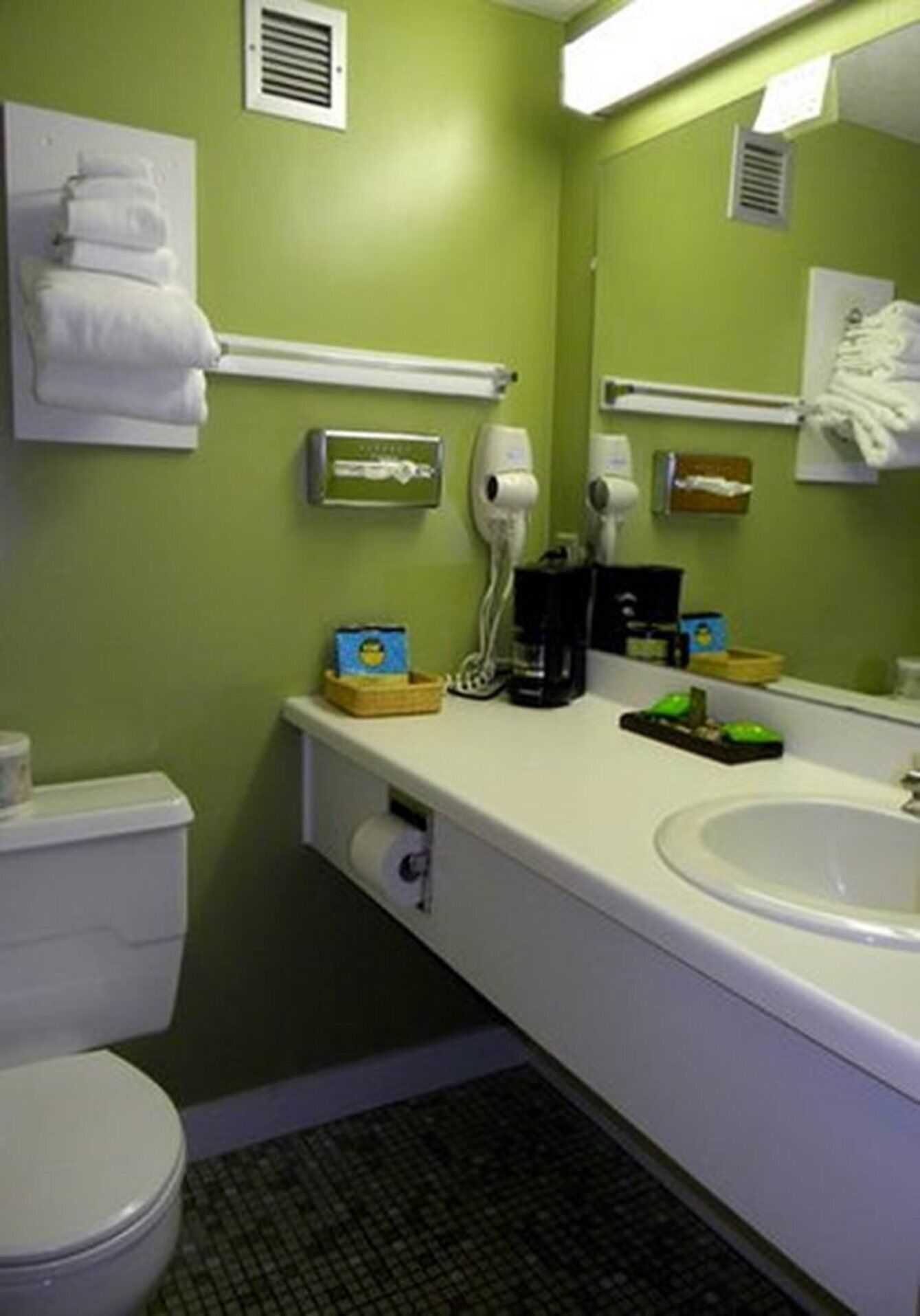 A bathroom with a white sink, green walls, a white toilet, and a mirror.