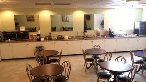 A hotel kitchen with multiple dining tables and chairs, a coffee machine, and a refrigerator.