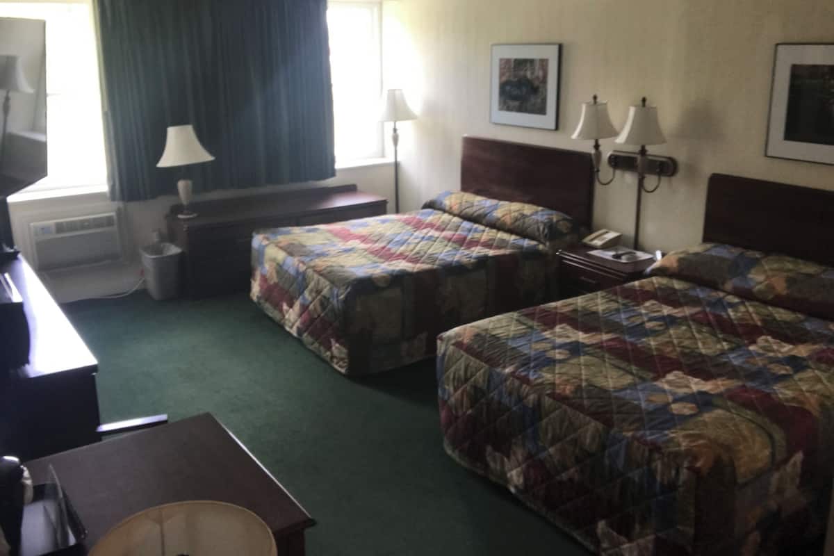 A hotel room with two beds, a desk, a chair, a lamp, a picture on the wall, and a window with curtains.