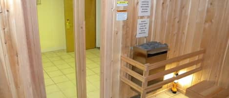 A wooden cabin with a small wooden bench and a shelf with a box. There are signs on the wall and a door leading to another room.