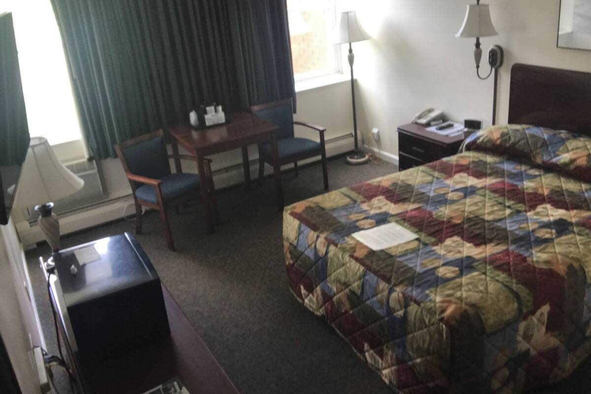 A hotel room with a bed, a desk, a chair, a lamp, and a telephone.